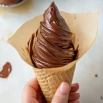 Hands shaping melted chocolate into cones on parchment paper.