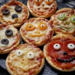 A plate of Halloween mini pizzas decorated with spooky and silly faces made from cheese, olives, and peppers
