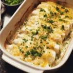 Baked white chicken enchiladas topped with melted cheese and fresh herbs in a white casserole dish