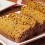 Close-up of sliced super moist pumpkin bread on a white plate, showing soft texture and rich golden-brown color